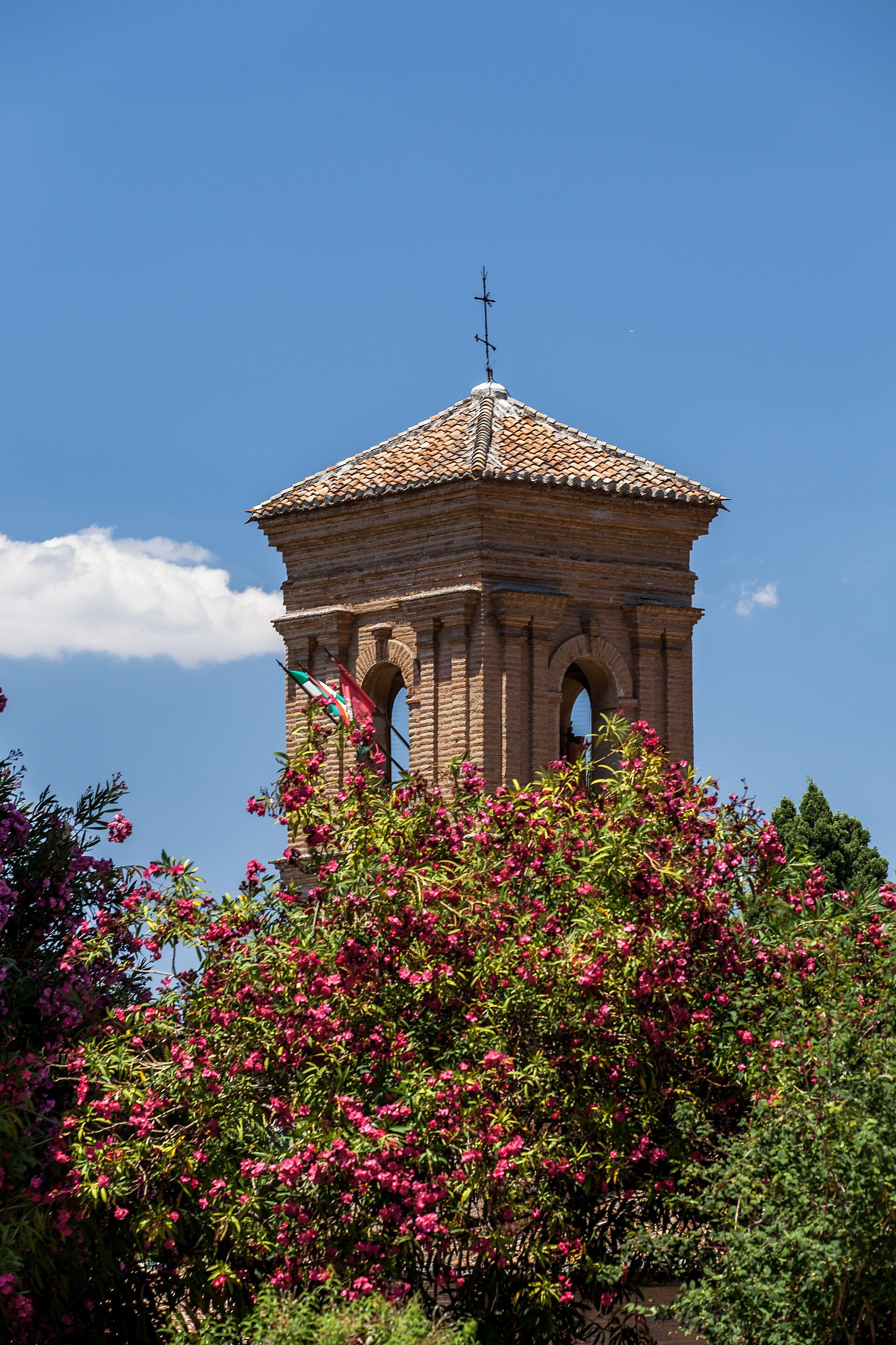 Alt text: Brick tower with arched windows, surrounded by vibrant pink flowers, under a clear blue sky.